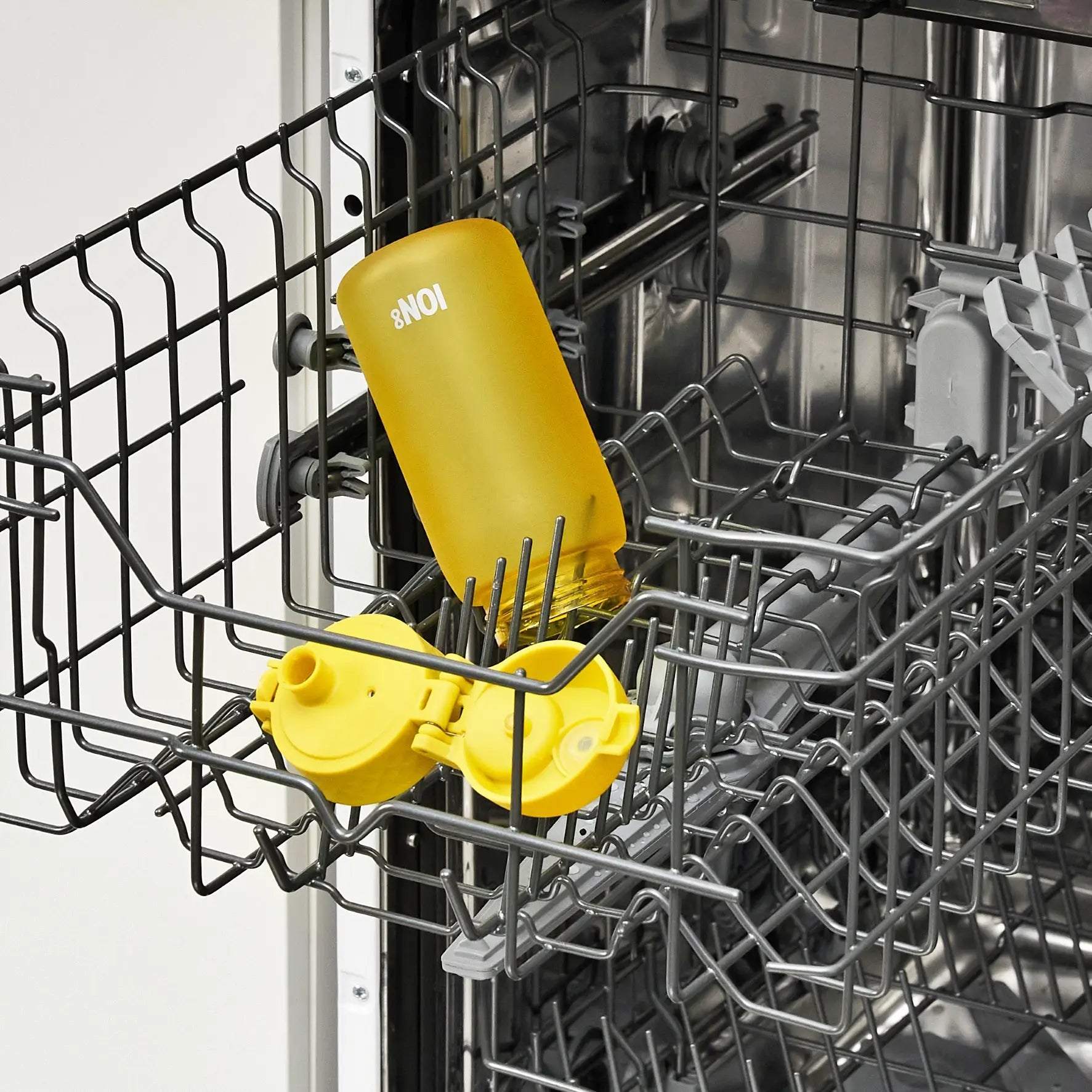 A yellow ION8 water bottle and its lid are being washed inside a dishwasher's top rack.