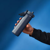 A dark gray water bottle stands upright with a flip-top lid and textured grip on a plain white background. Branding on the bottle reads ION8.