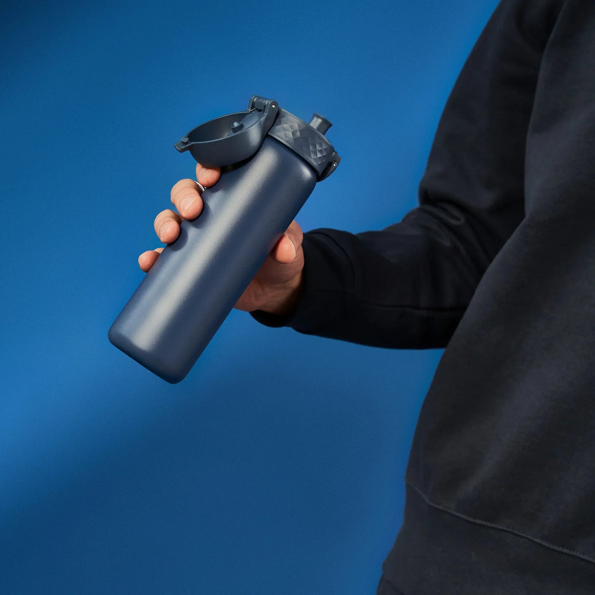 A dark gray water bottle stands upright with a flip-top lid and textured grip on a plain white background. Branding on the bottle reads ION8.