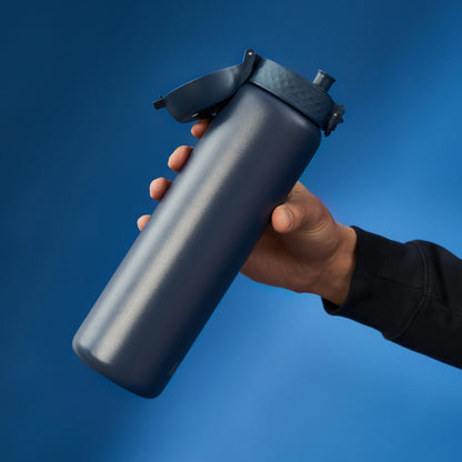 Hand holding a blue insulated water bottle with a flip-top lid against a solid blue background.