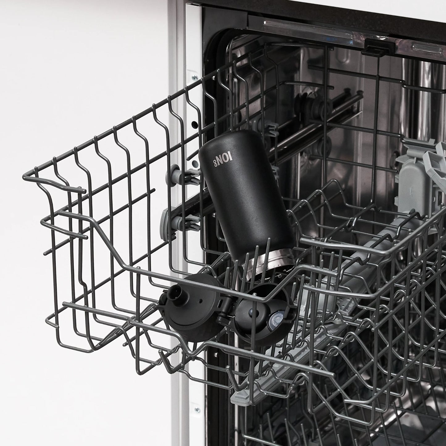 A black reusable bottle labeled "ION8" sits inside an open dishwasher's upper rack amidst a kitchen setting.