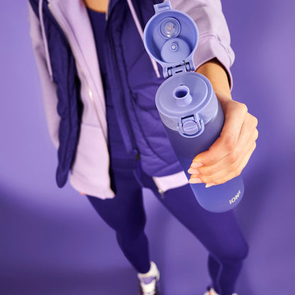 A hand holds a purple water bottle with an open flip-top cap in a purple-themed environment. The word "ION8" is visible on the bottle.