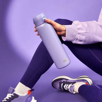 A lavender-colored water bottle labeled "ION8" is held in a hand wearing a purple sweatshirt sitting cross-legged, surrounded by a matching purple athletic outfit and sneakers against a purple backdrop.