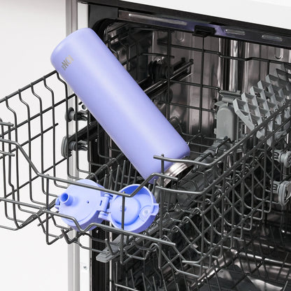 A blue water bottle marked "8NCJ" sits open inside a dishwasher's upper rack surrounded by metal prongs and gray plastic components.