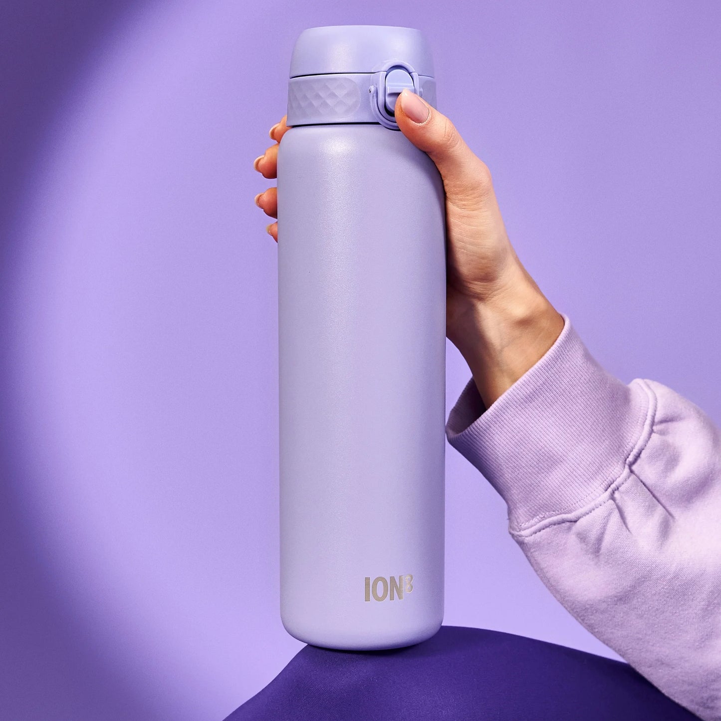 A hand holds a lavender water bottle with the text "ION8" against a matching purple background wearing a lavender sleeve.