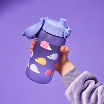 A hand holds a purple water bottle decorated with colorful hedgehog illustrations against a matching purple background