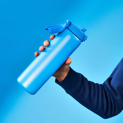 A hand holds a blue water bottle with a flip-top lid against a solid blue background creating a matching color theme.