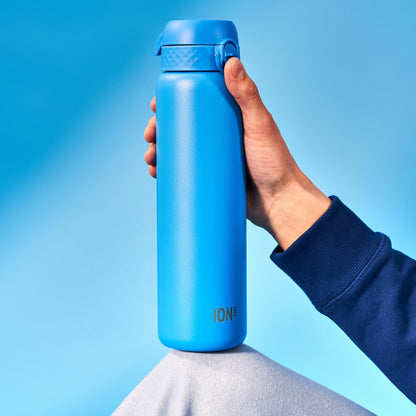 A blue water bottle labeled "ION8" is held vertically by a hand against a blue background with a knee in view.