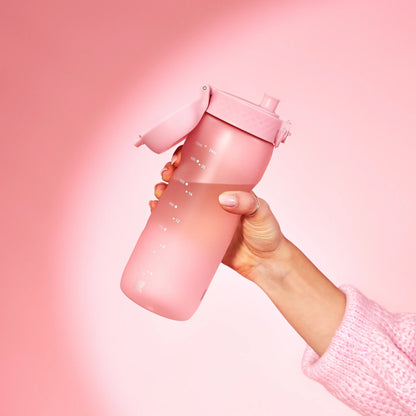 A pink water bottle is held by a hand wearing a pink sweater against a pink background with measurement markings ranging from 250ml to 240ml.