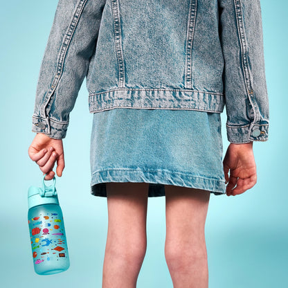 A child wears a denim jacket and skirt holding a blue water bottle with colorful aquatic designs against a bright blue background.