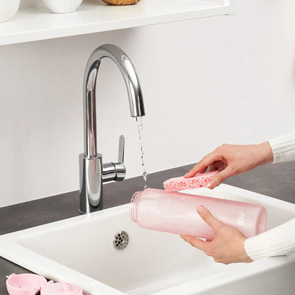 Hands hold a pink bottle labeled "ION8" while cleaning it with a sponge under running water from a silver faucet in a white sink countertop setting.