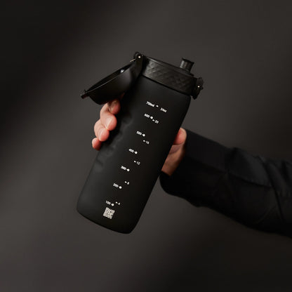 A person holds a black water bottle with a flip-top lid against a dark background. Measurement markings and a QR code are visible: 750 ml to 100 ml, 24 oz to 4 oz.