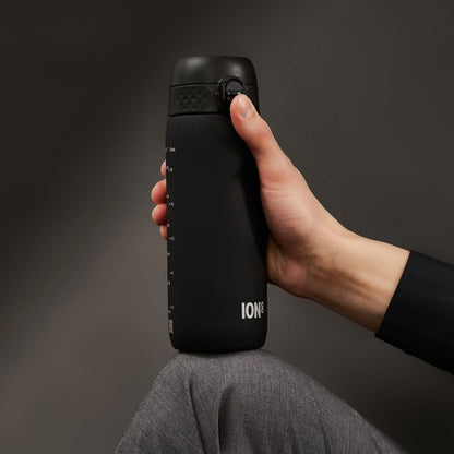 A black water bottle held by a hand rests on a knee in a dimly lit environment. The bottle features measuring marks and the text "ION8".