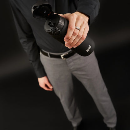 A person wearing a black shirt and gray pants holds an open black water bottle labeled "ION8" in a dark setting.