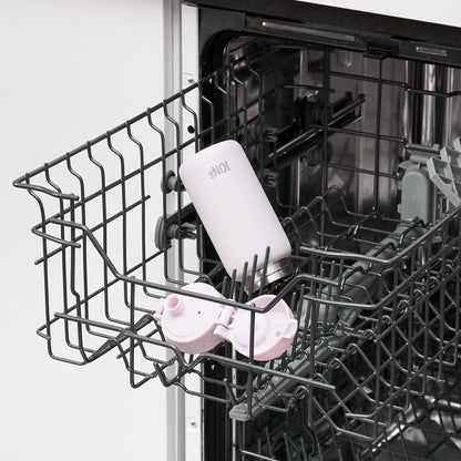 A white bottle labeled "8NOI" and a pink lid are placed inside an open dishwasher rack in a kitchen environment.