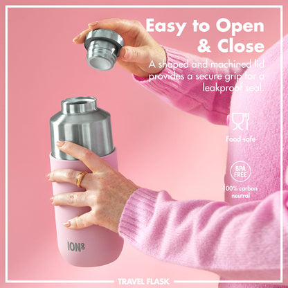 A person unscrews the lid of a pink and metal travel flask in a pink environment. Text: Easy to Open & Close A shaped and machined lid provides a secure grip for a leakproof seal Food safe BPA FREE 100% carbon neutral ION8 TRAVEL FLASK