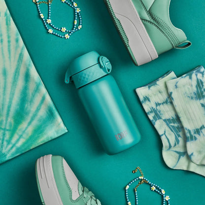 A turquoise water bottle labeled "ION8" rests on a green surface surrounded by matching sneakers, tie-dye socks, a shirt, and floral jewelry.